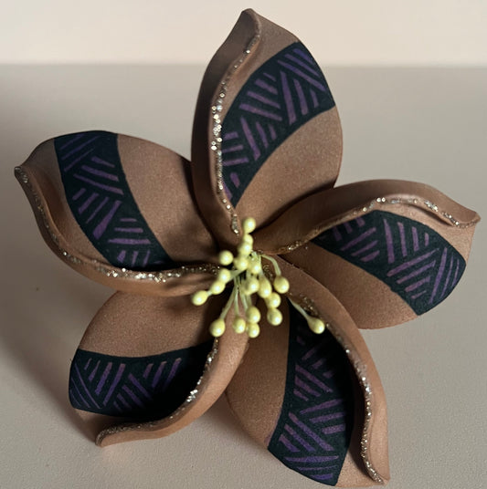 Fleur décorative à cinq pétales en mousse de couleur marron chocolat, ornée de motifs géométriques noirs et violets sur chaque pétale. Les bords des pétales sont soulignés de paillettes dorées. Le centre de la fleur est décoré de petits pistils jaunes en perles, apportant une touche délicate et réaliste à l’ensemble.