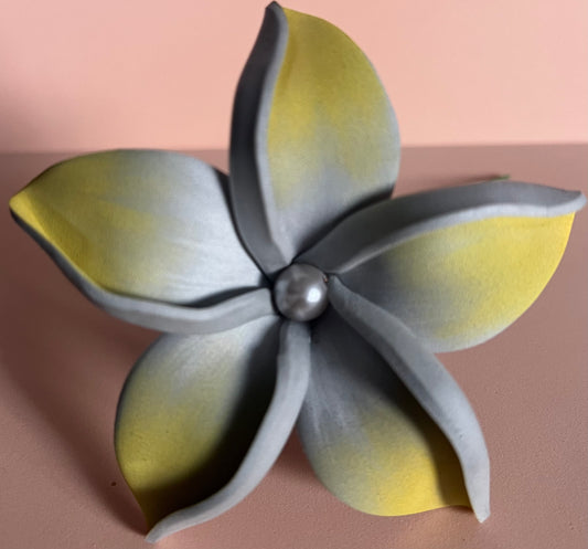 Fleur artificielle à cinq pétales en dégradé de gris et de jaune, ornée d’une perle au centre. L’arrière-plan est rose pâle, créant un contraste doux avec les couleurs de la fleur.